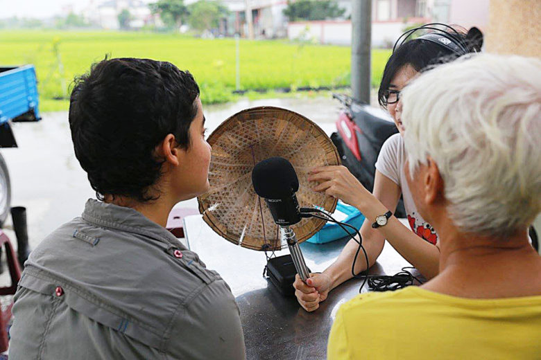 某次收音時卻遇上蘭陽平原的午後雷陣雨，大米便趕緊拿起斗笠擋風遮雨，也避免風雨聲干擾，也算是難得奇觀。（圖／田文社提供）