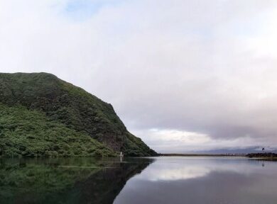 龜山島龜尾湖涼亭一側視野，湖為山坡環繞，彼側為海堤下的舊聚落遺址，遠景可見台灣本島(攝影/馮孟婕)