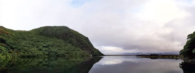 龜山島龜尾湖涼亭一側視野，湖為山坡環繞，彼側為海堤下的舊聚落遺址，遠景可見台灣本島(攝影/馮孟婕)