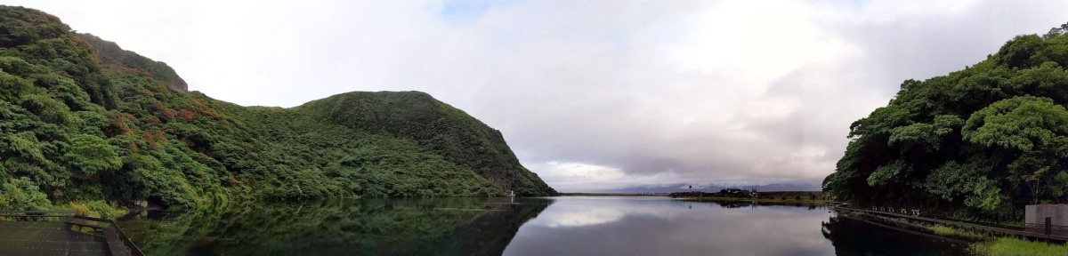 龜山島龜尾湖涼亭一側視野，湖為山坡環繞，彼側為海堤下的舊聚落遺址，遠景可見台灣本島(攝影/馮孟婕)